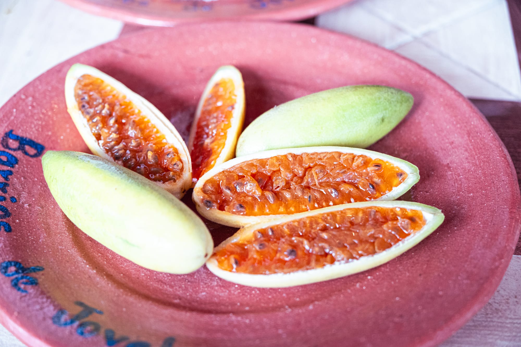 Sliced banana passionfruit arranged on a red clay plate, showing their bright orange, jelly-like interior