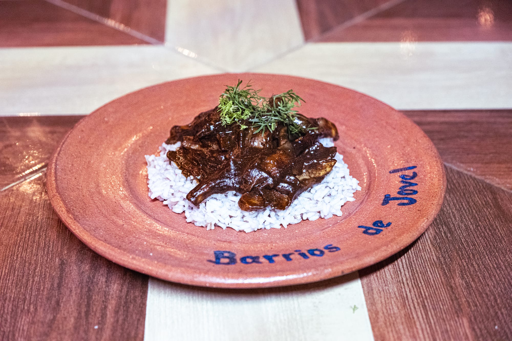 A clay plate labeled “Barrios de Jovel” holding a serving of oyster mushroom mole over white rice, garnished with fresh herbs