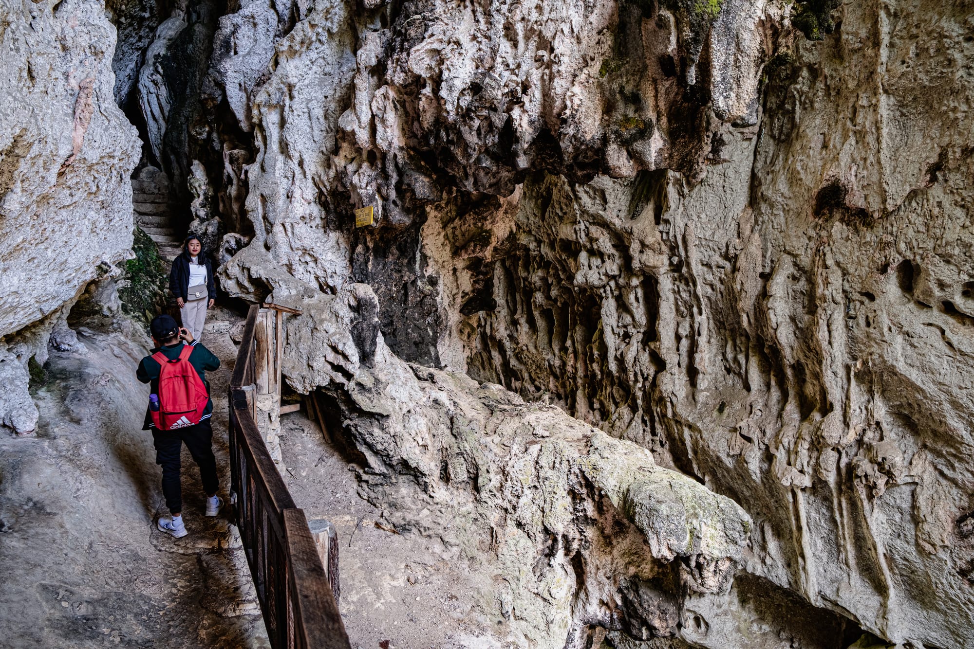 Visitors walking along a narrow limestone walkway inside the caves at El Arcotete near San Cristóbal de las Casas, surrounded by rugged rock formations and carved walls