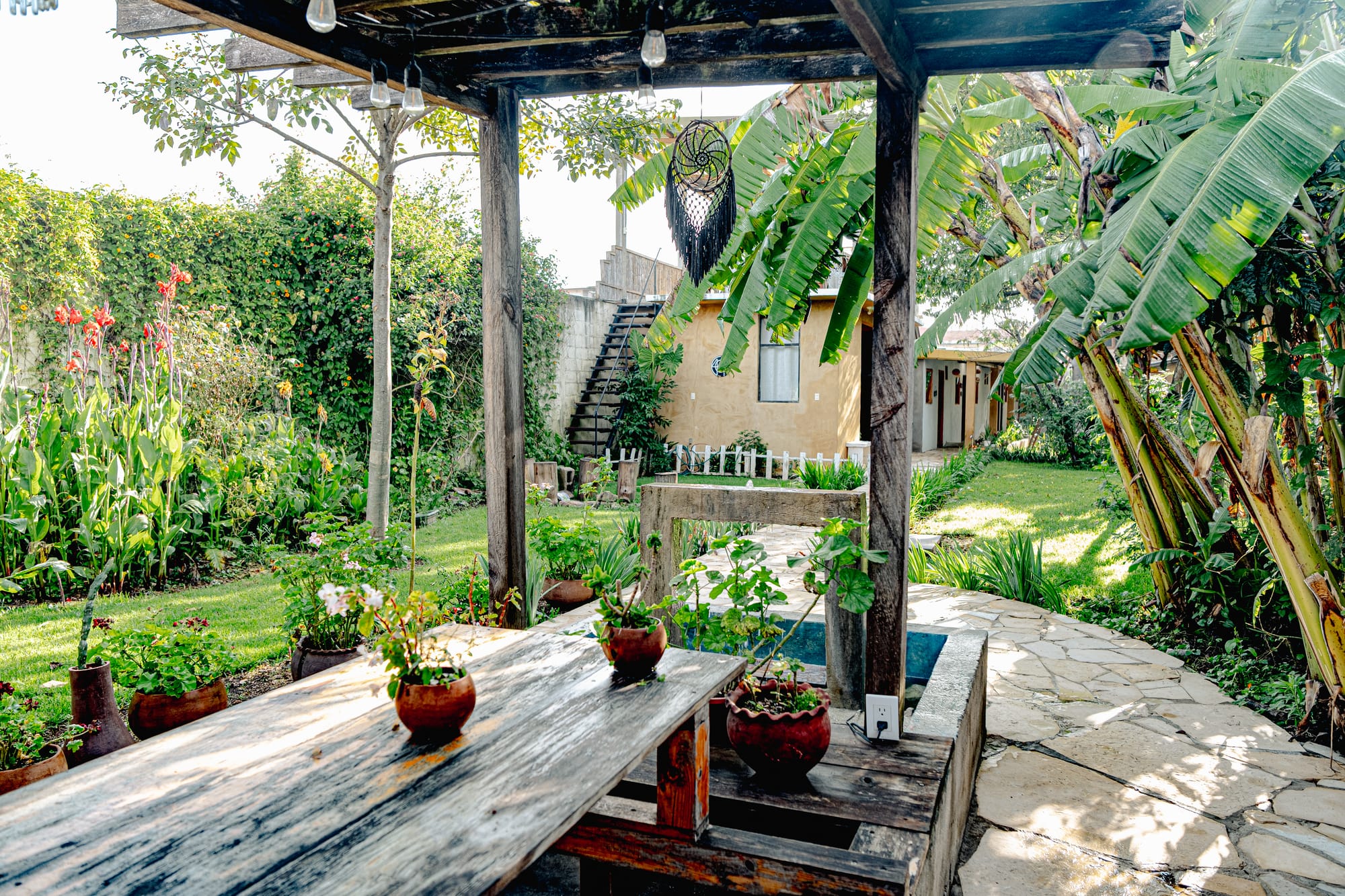 Outdoor garden seating area at Co404 coliving in San Cristóbal de las Casas, surrounded by tropical plants, banana trees, and stone pathways