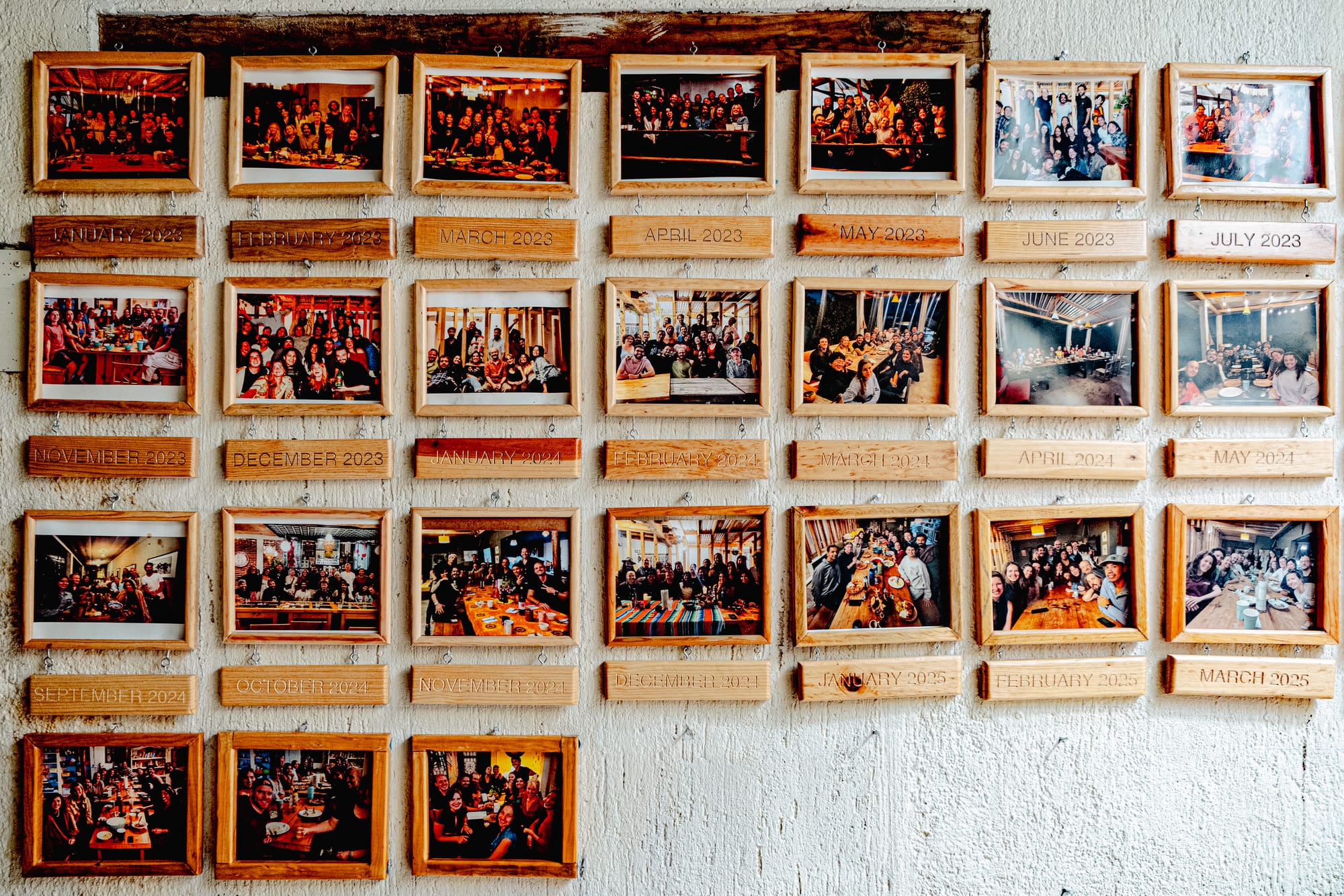 Photo wall at Co404 coliving in San Cristóbal de las Casas, displaying monthly group pictures of residents gathered for events and community activities