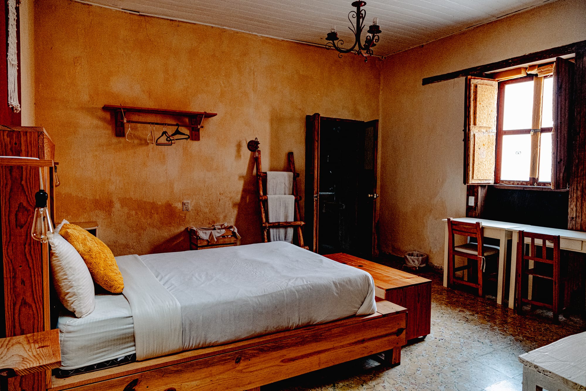 Private room at Co404 coliving in San Cristóbal de las Casas, featuring a wooden bed, natural light, rustic walls, and a work desk for digital nomads