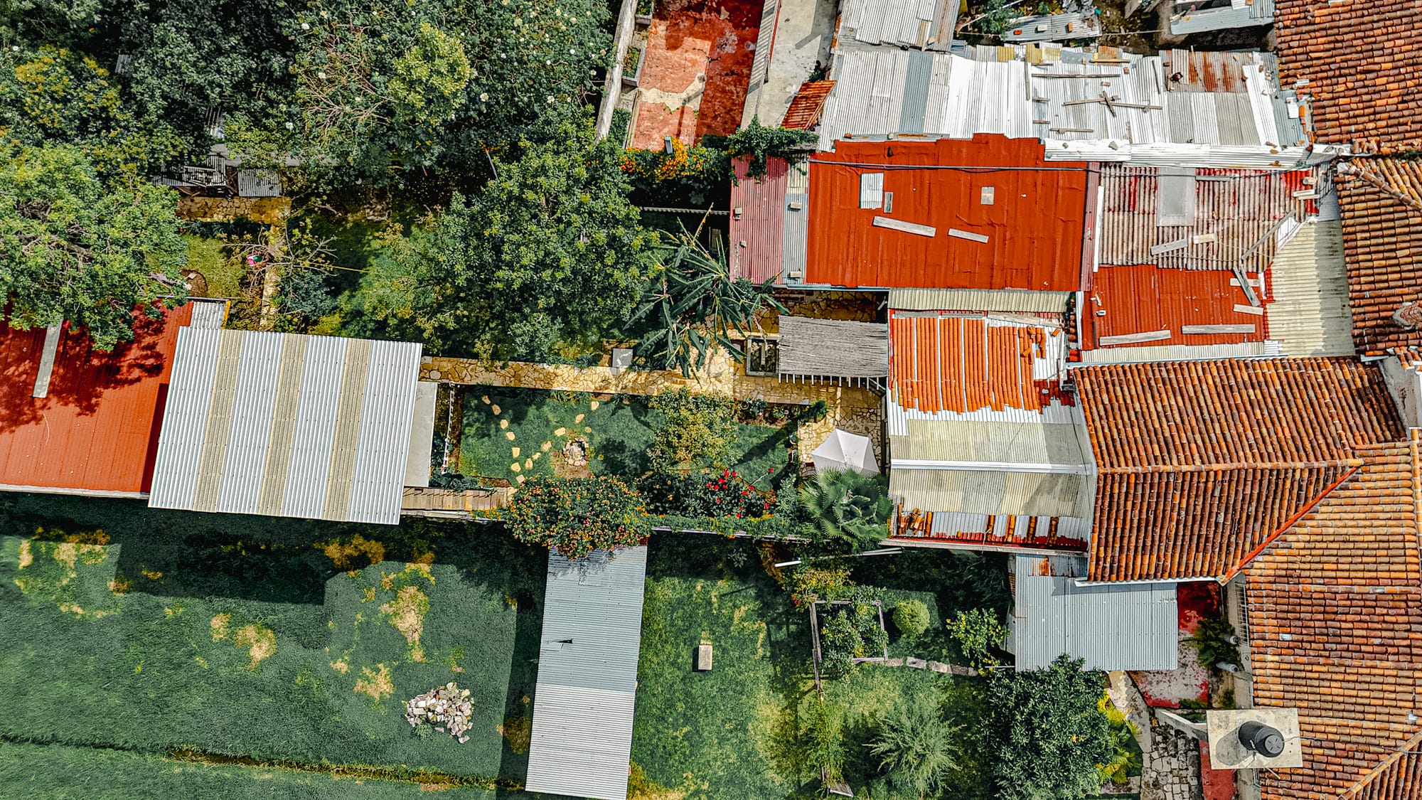 Drone view of Co404 coliving in San Cristóbal de las Casas, showing the garden, pathways, rooftop terrace, and surrounding neighborhood from above