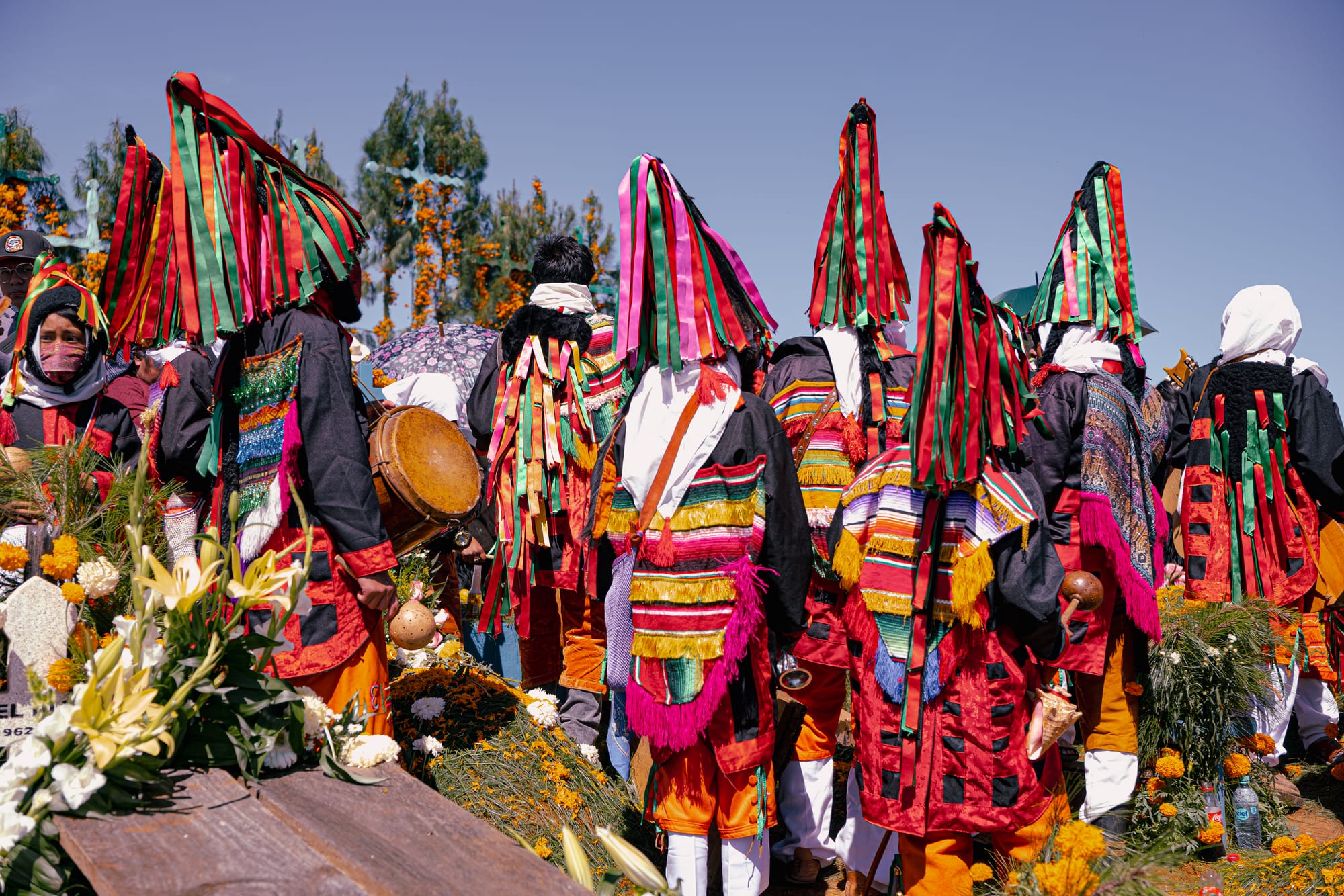 Indigenous Day of the Dead ceremony in Chiapas, Mexico, traditional dancers wearing colorful woven clothing and ribbon headdresses, marigold-covered graves at Romerillo Cemetery near San Cristóbal de las Casas, local Día de Muertos ritual with music, offerings, and community gathering