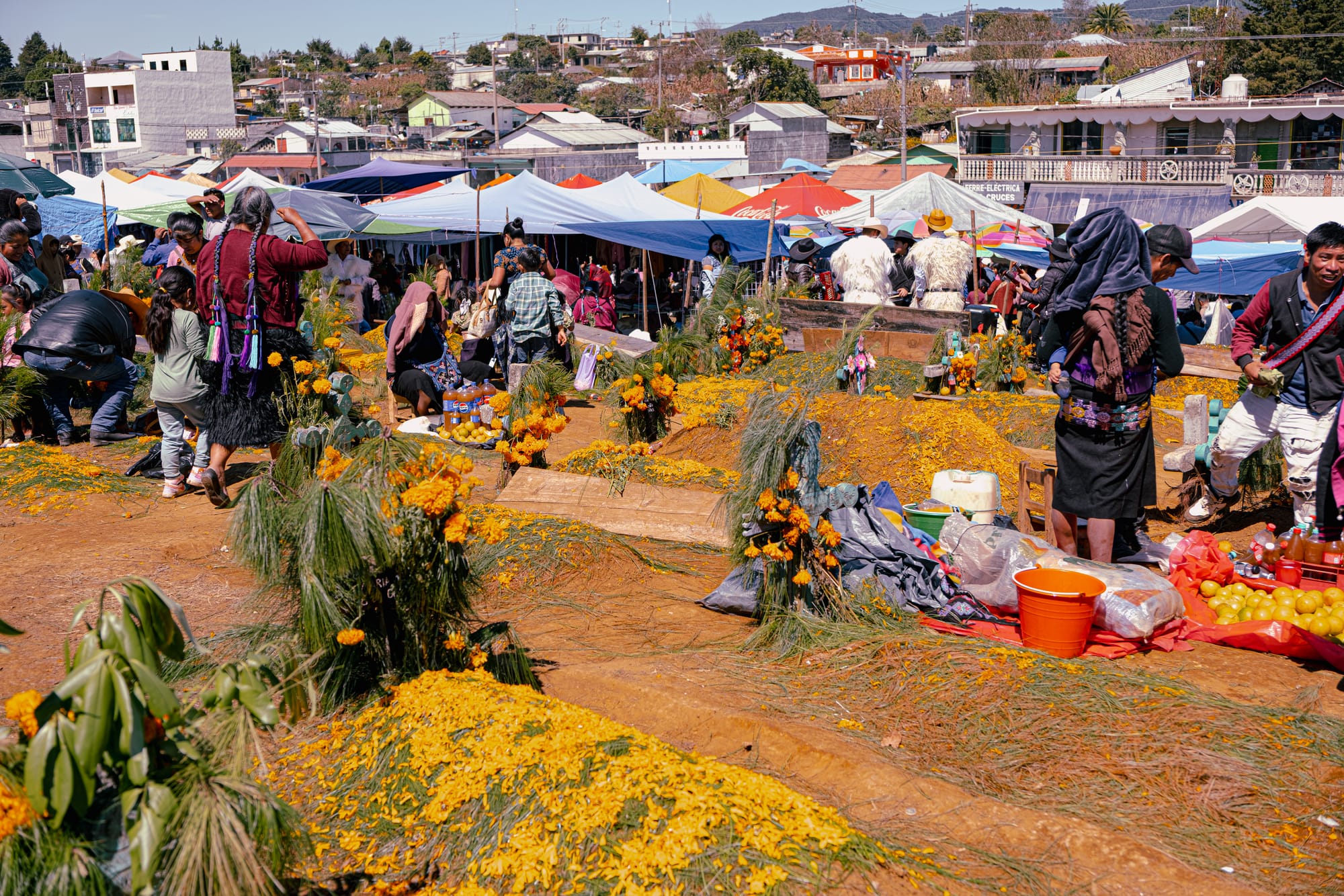 Día de Muertos at Romerillo Cemetery Chiapas, crowded hilltop cemetery filled with pine covered graves and marigold mounds, families arranging offerings and spending the day together, wooden crosses and shallow tombs packed closely, market tents and food stalls surrounding the cemetery, indigenous Day of the Dead celebration near San Cristóbal de las Casas