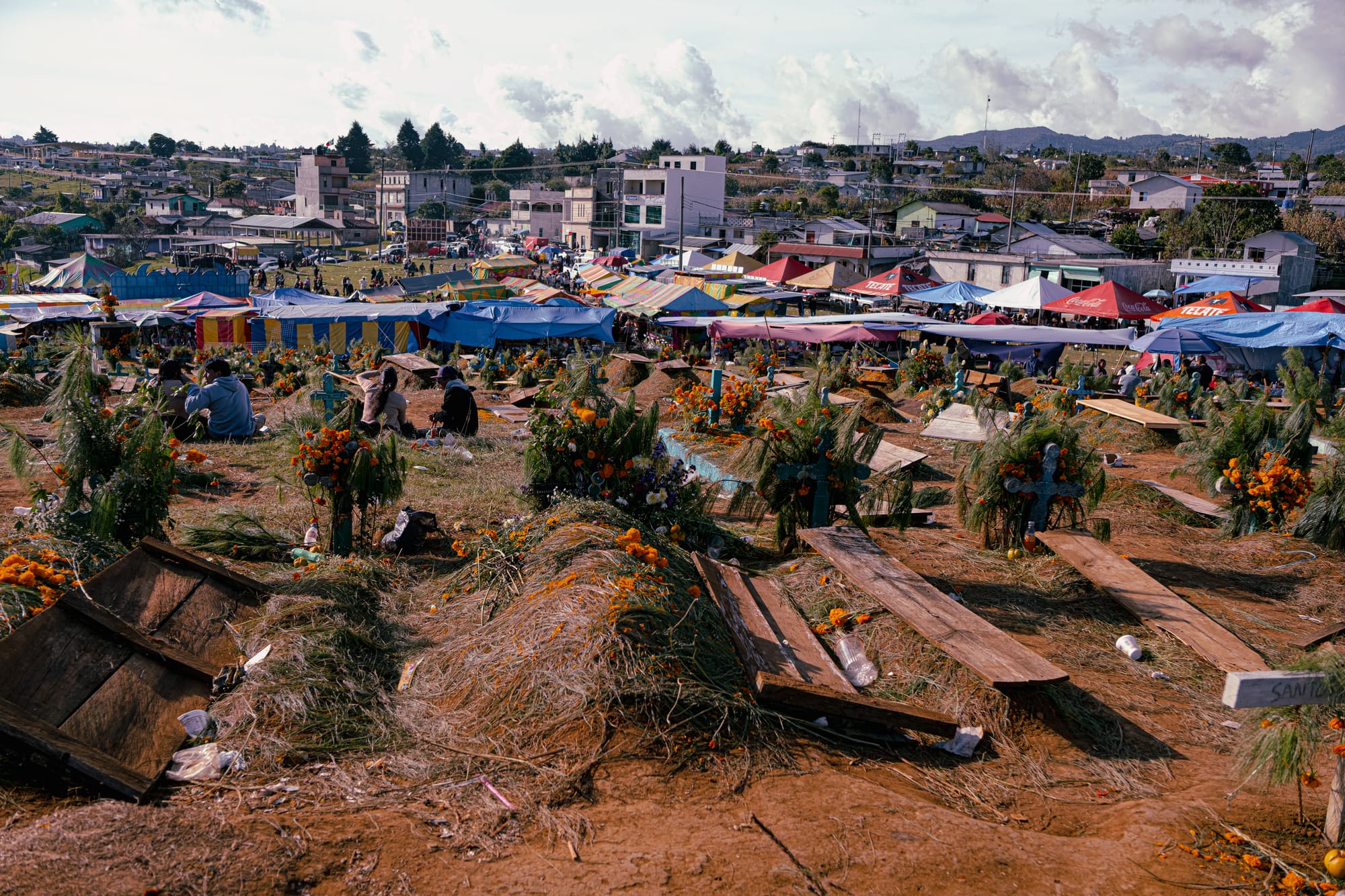 Día de Muertos at Romerillo Cemetery Chiapas, wide panoramic view of hilltop cemetery with pine covered graves and marigold decorated wooden crosses, families sitting among graves during Day of the Dead, market tents and festival stalls surrounding the cemetery, local indigenous burial traditions near San Cristóbal de las Casas