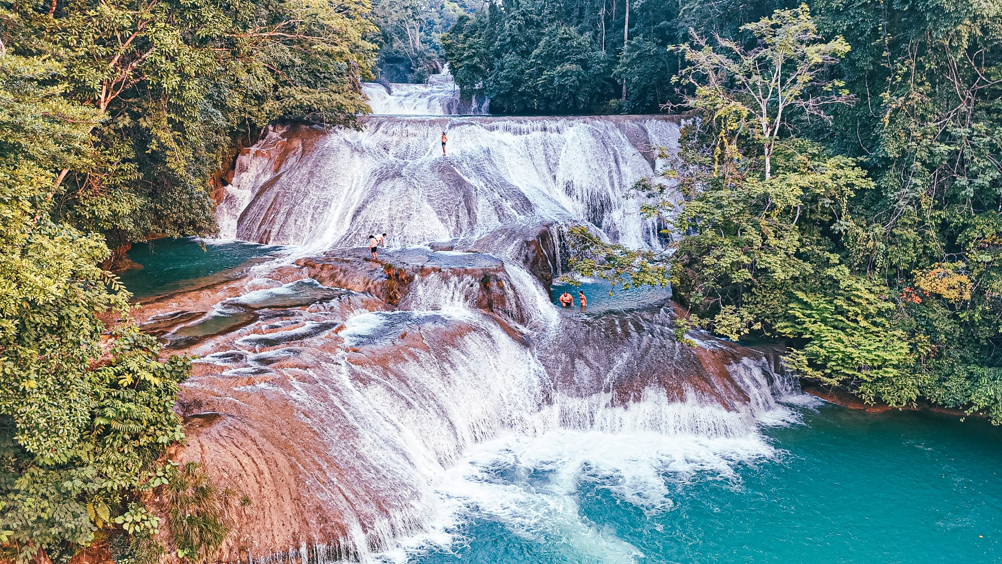 Roberto Barrios waterfalls near Palenque, Chiapas, showing wide multi-tiered cascades flowing over smooth limestone rock into turquoise natural pools, with visitors swimming and standing on the rock formations, highlighting the expansive waterfall system often considered one of the most impressive waterfalls near Palenque in southern Mexico
