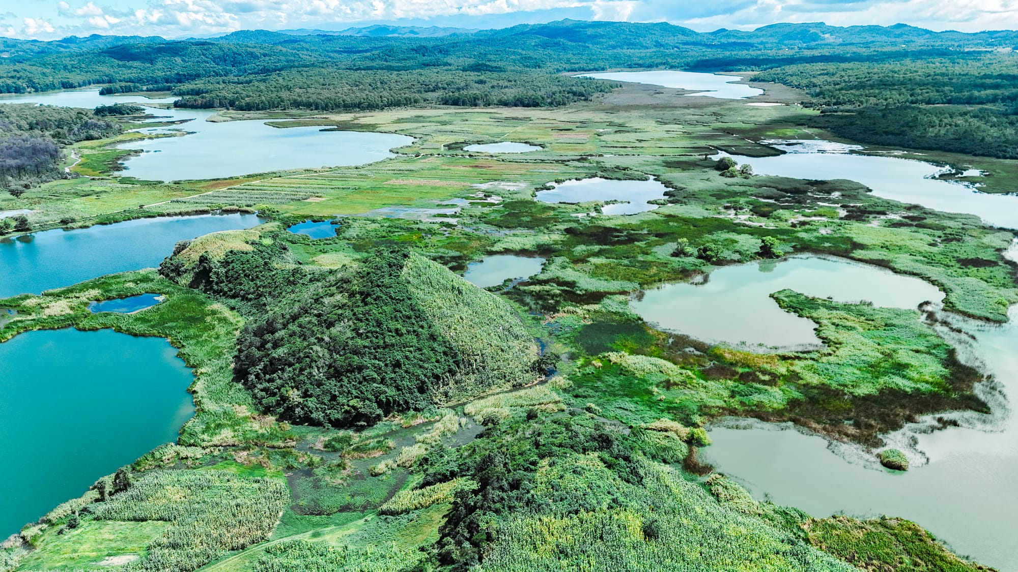 Aerial panorama of Montebello Lakes in Chiapas, showing multiple turquoise lakes, wetland patches, and forested hills stretching toward the Guatemala border
