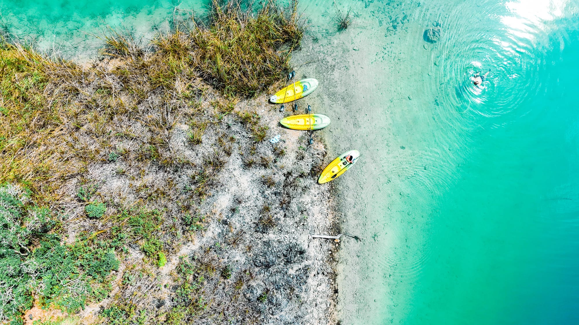 Aerial view of Montebello Lakes in Chiapas showing kayaks on the rocky shore and a person swimming in the bright turquoise water near the edge of the lake