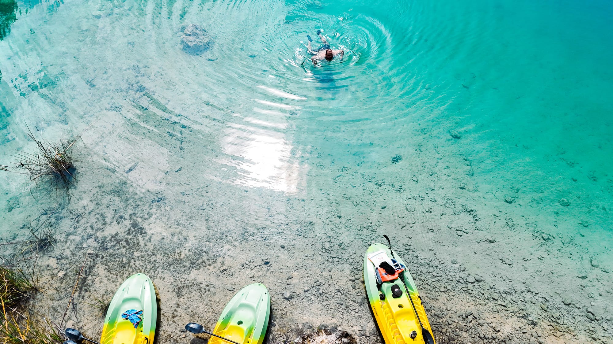 Clear turquoise shallows at Montebello Lakes in Chiapas with kayaks pulled onto the rocky shore and a swimmer creating ripples in the bright water