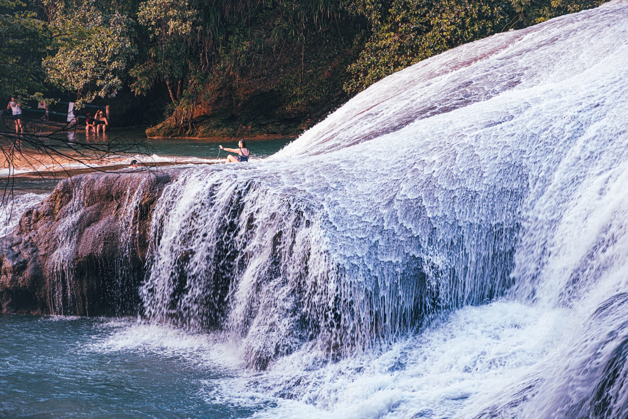 Cascadas Roberto Barrios waterfalls near Palenque, Chiapas, Mexico, person sitting on limestone waterfall edge, water flowing over wide cascades, walkable waterfalls and swimming pools, jungle waterfalls Roberto Barrios day trip near Palenque
