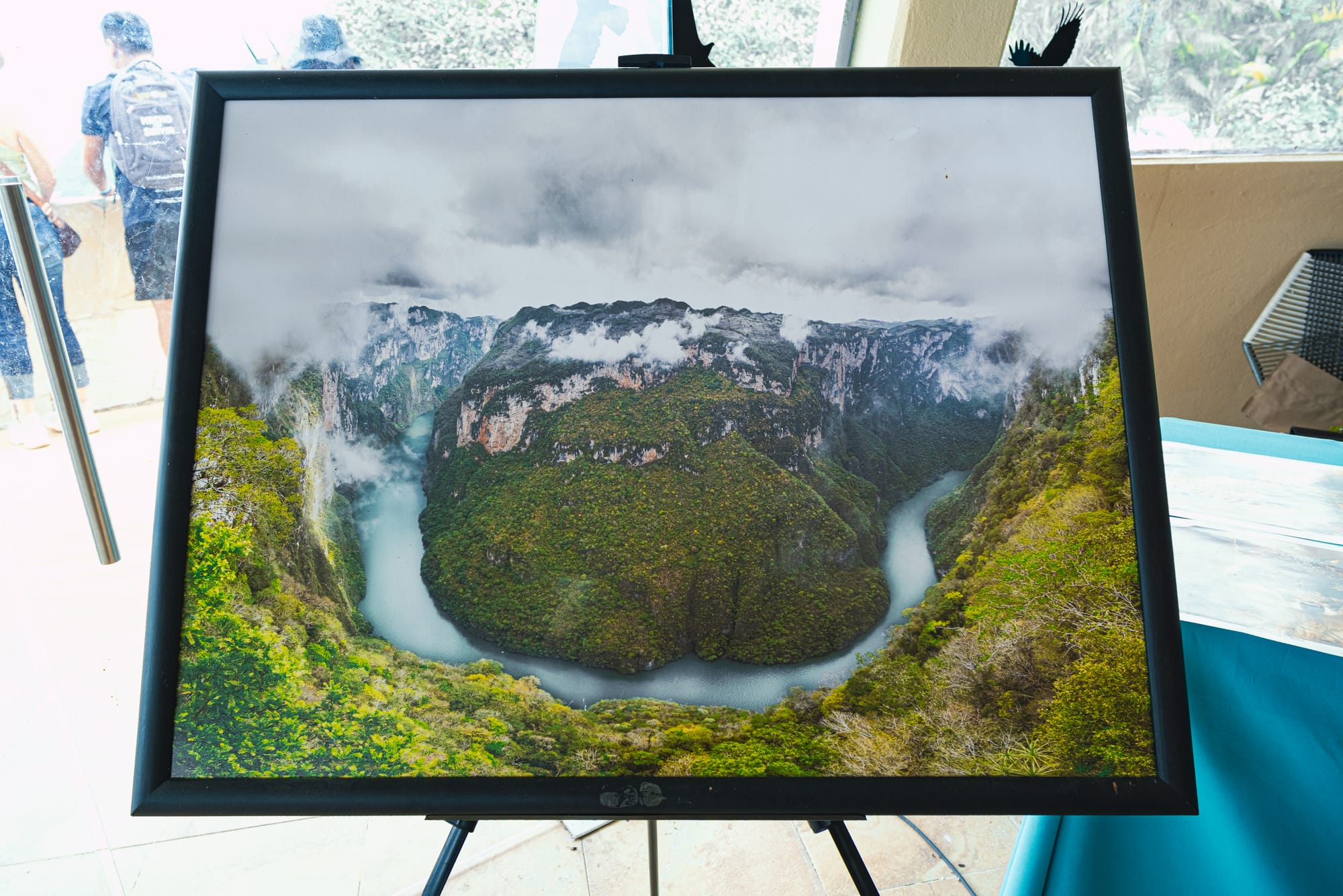 Framed photograph of Sumidero Canyon displayed at the lookout, showing the Grijalva River looping around steep green cliffs under low clouds