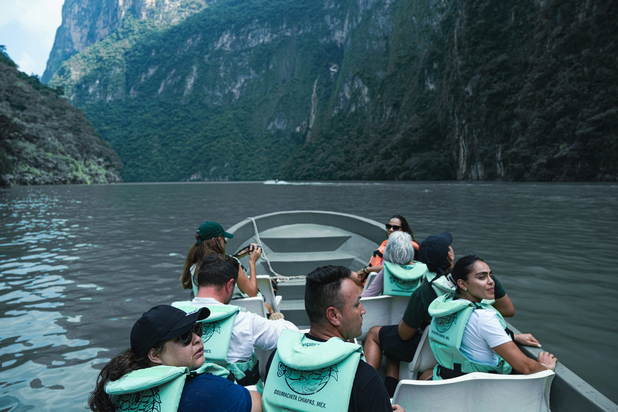 Passengers riding through Sumidero Canyon on a boat tour, surrounded by towering green cliffs and the calm waters of the Grijalva River