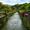 Lush canal in Furnas lined with stone walls, flowering plants, and forested hills in the background