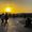 People gather at sunset in Karaalioğlu Park, Antalya, with golden light over the mountains, city skyline, and a street musician playing in the foreground