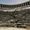 Visitors sit scattered across the steep, curved stone seating of the ancient Aspendos amphitheater under a hazy sky