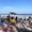 Families and children gather on Diani Beach near an ice cream vendor’s cart, with people swimming and playing in the Indian Ocean in the background under a clear blue sky