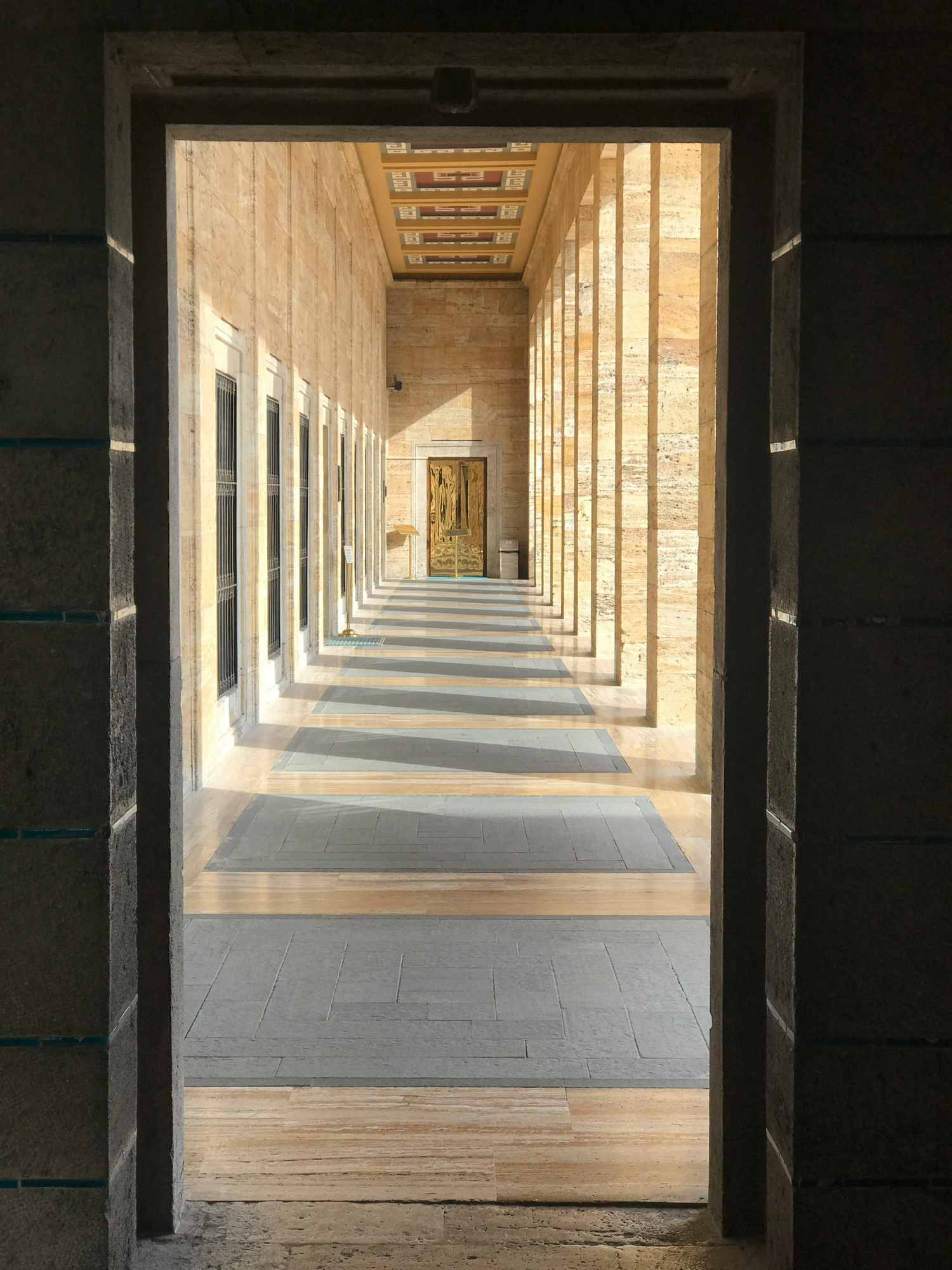 Sunlit stone corridor with repeating columns and distant doorway, expressing architectural order, symmetry, and calm institutional design.