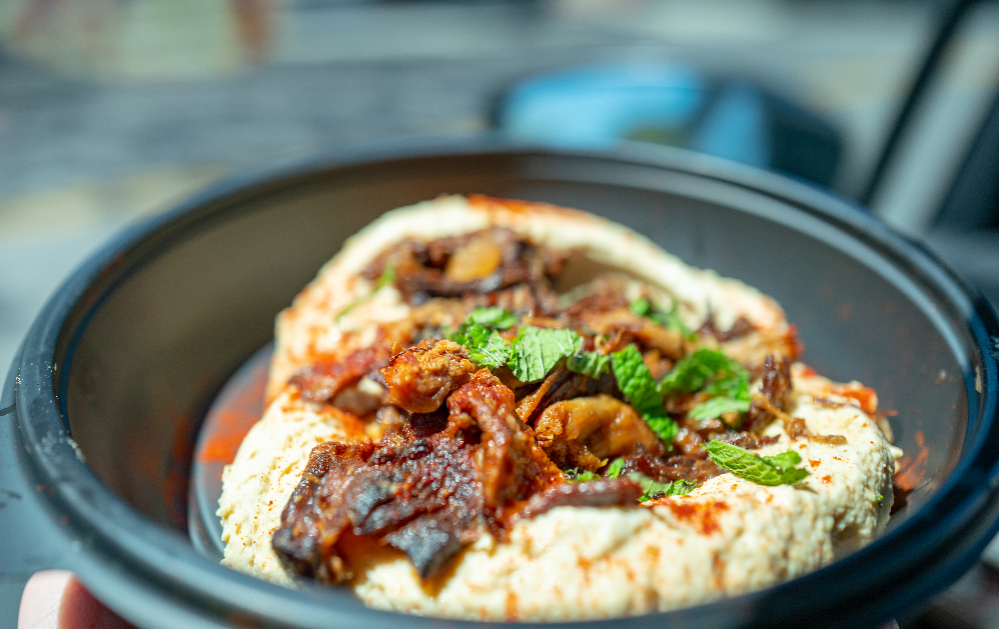 A bowl of hummus topped with herbs and strips of sundried tomatoes.