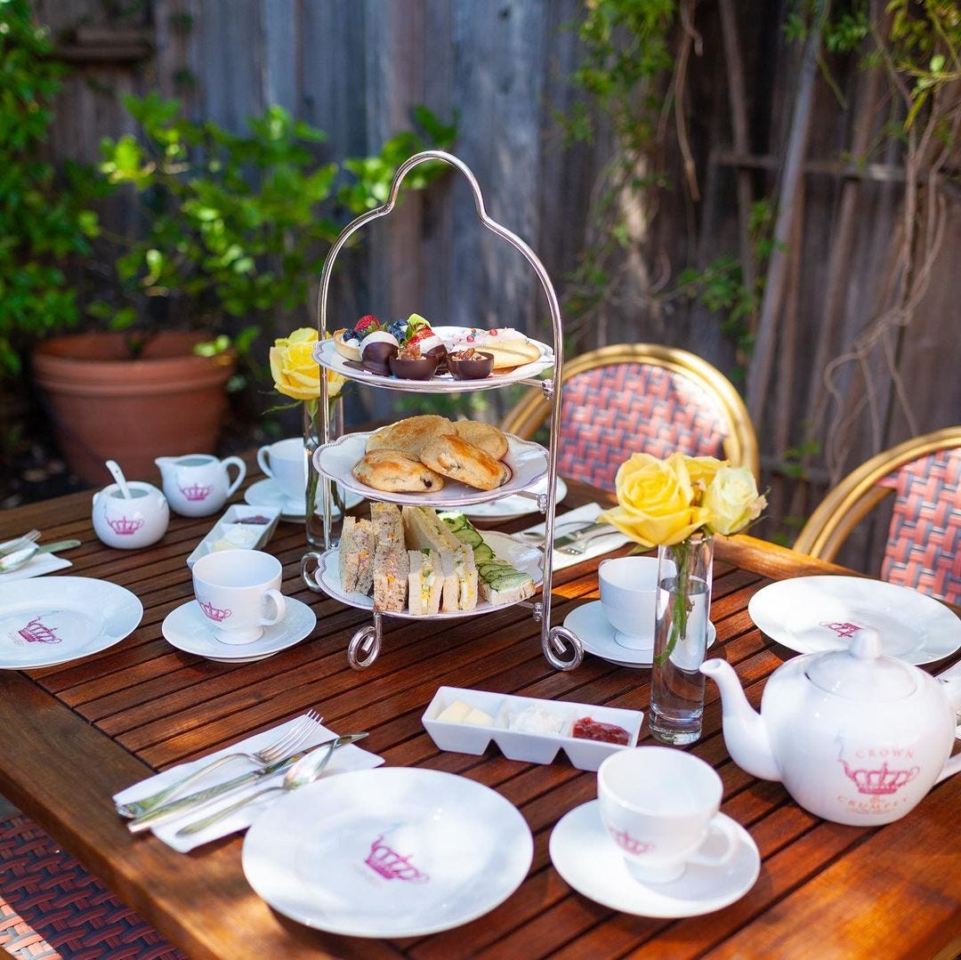 An outdoor dining table set for a tea party with a 3-tier dessert tray in the center.
