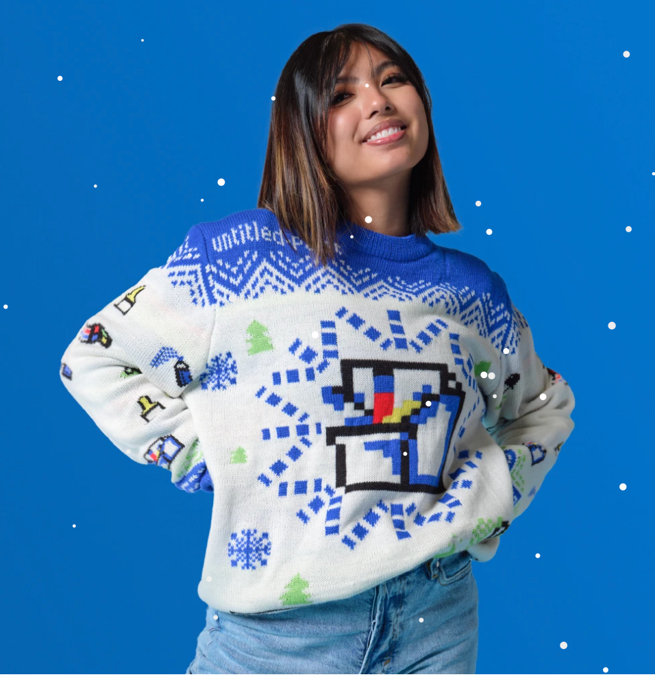 A brown person with shoulder-length bob wearing a white + blue sweater with the MS Paint logo in a snowflake.