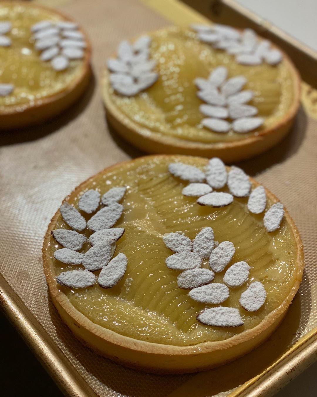 3 round pear tarts with sliced almonds arranged like fern leaves on each.
