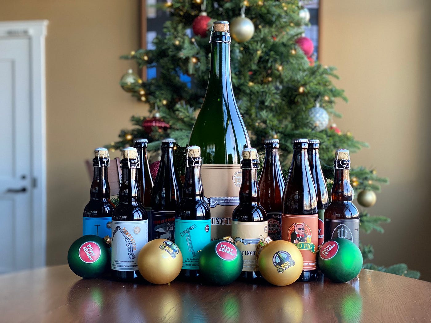 An assortment of small bottles of beer around a large one, all in front of a Christmas tree.
