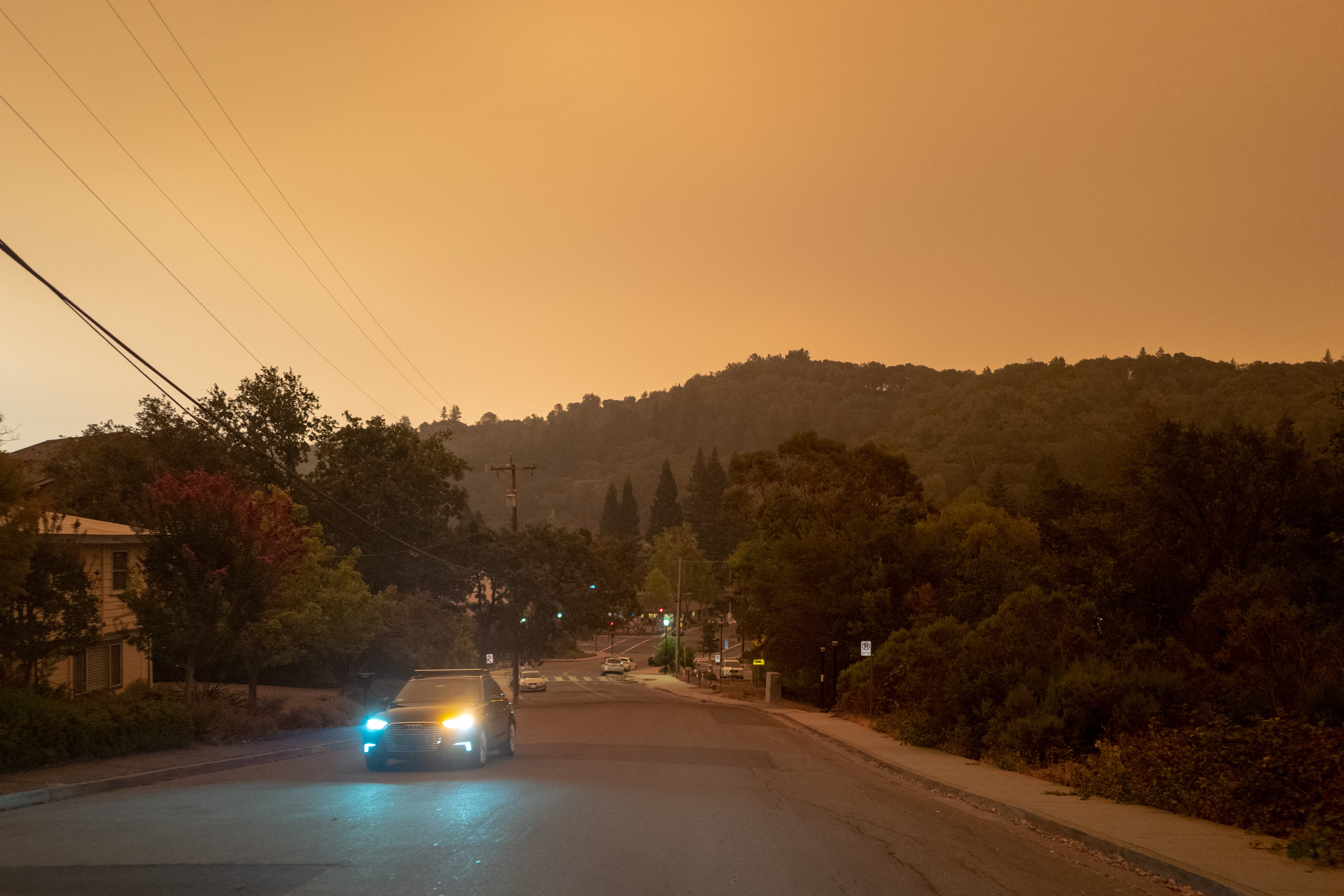 View down a suburban street with wooded hills in the background, under a smoky grayish-orange sky.