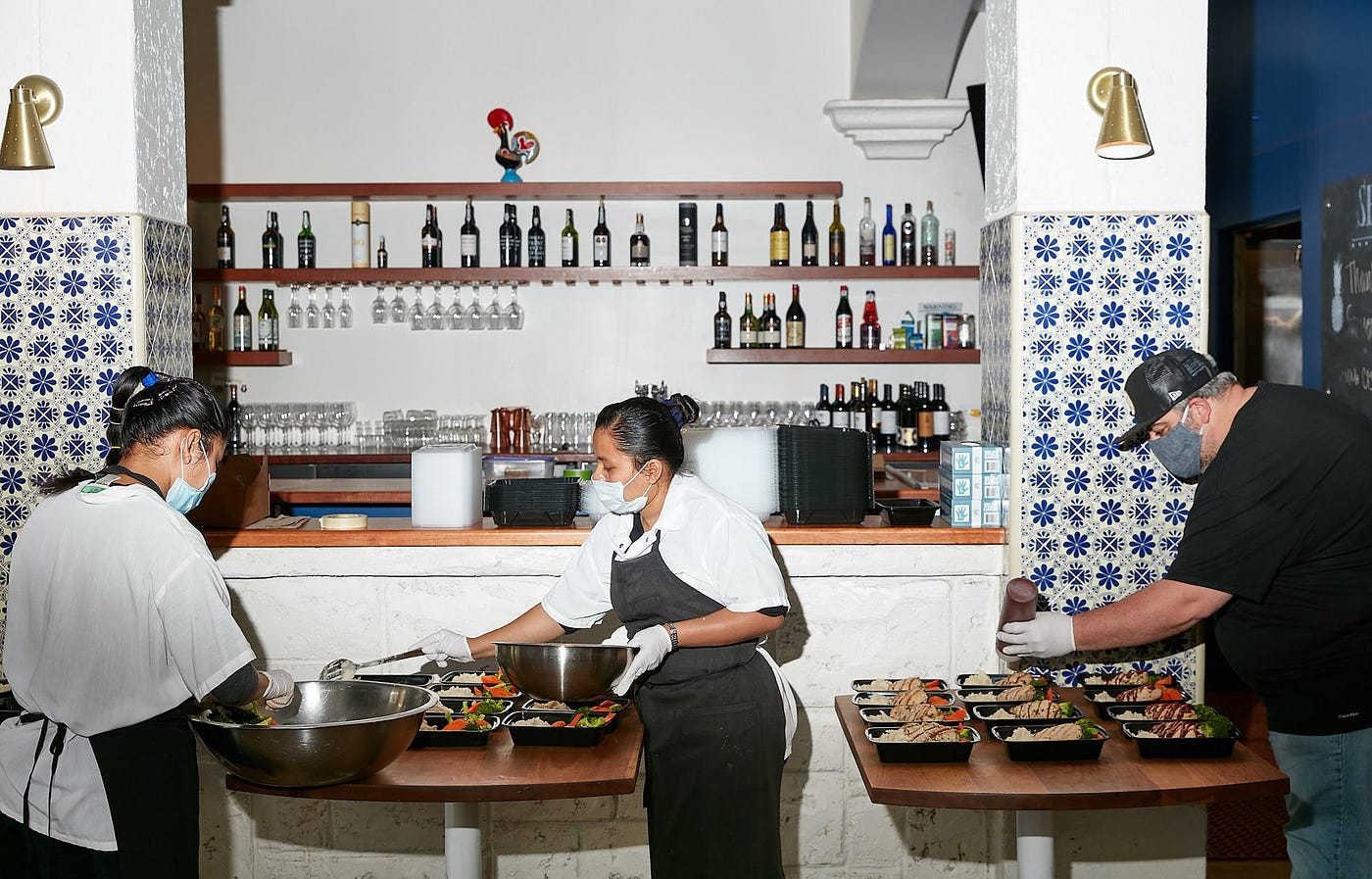 3 masked chefs preparing food in a kitchen.