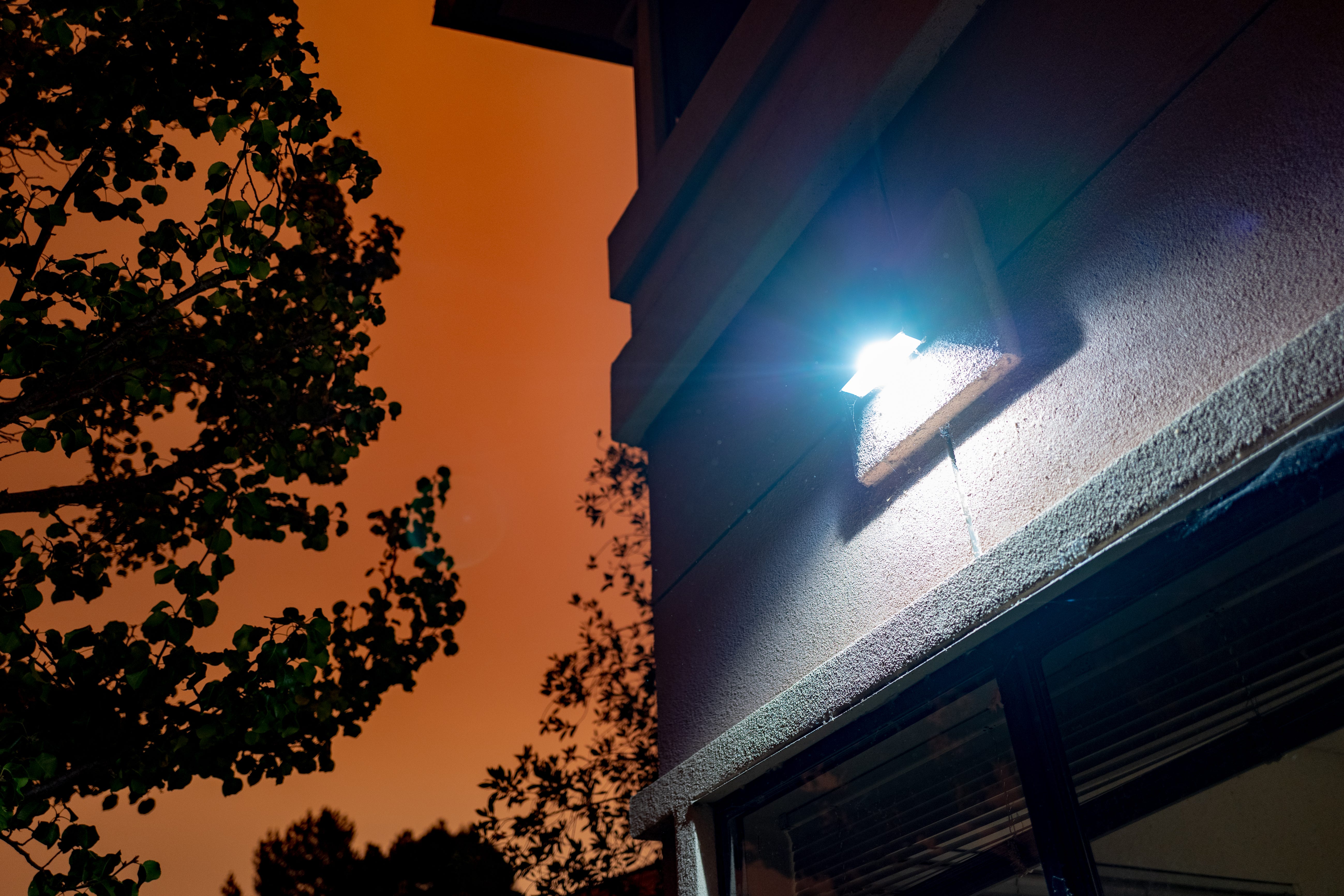 A porch light on on the side of a house, with a deep orange, smoky sky in the background.