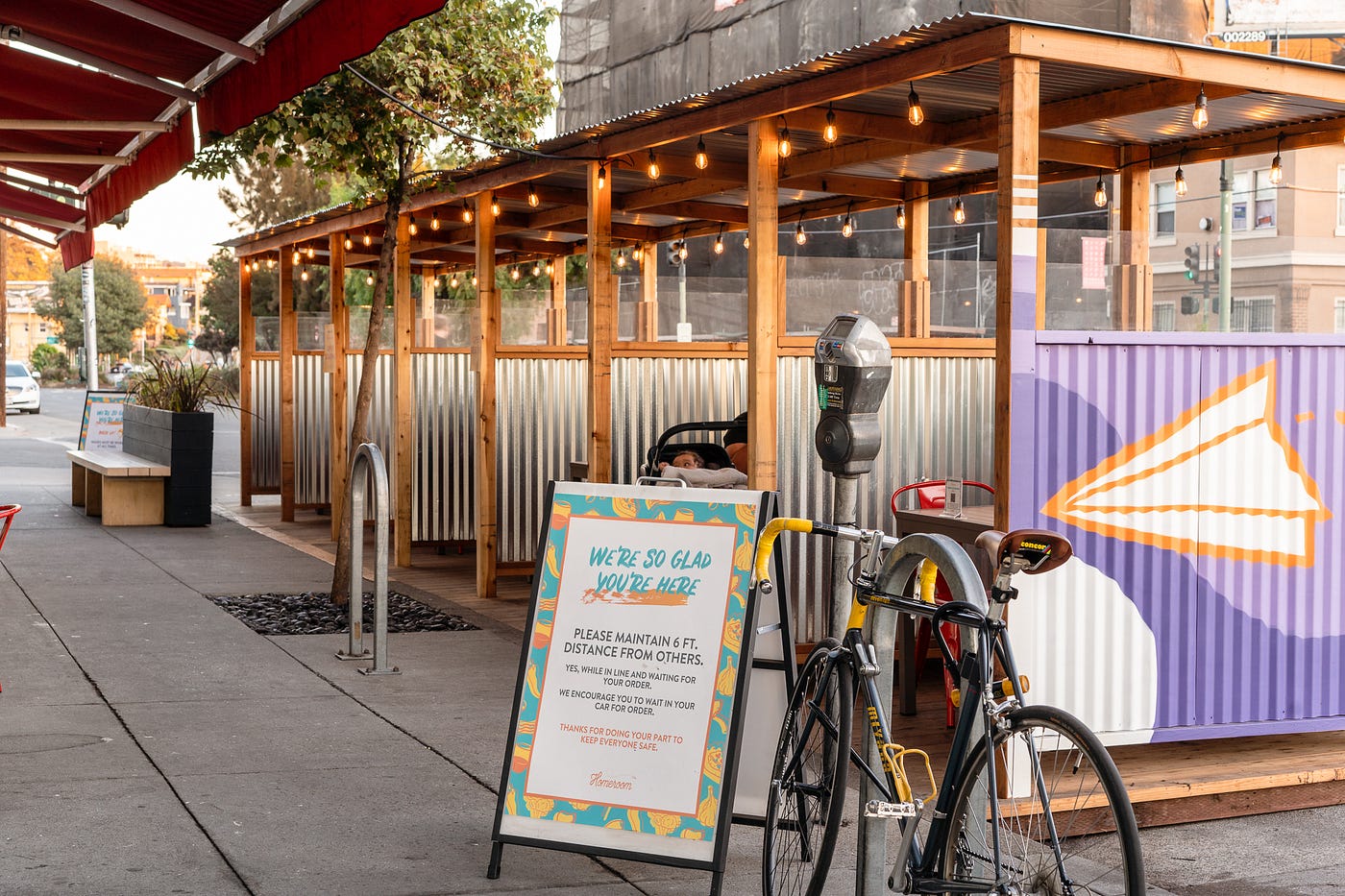 Outdoor dining at Homeroom: cubicles of corrugated metal with wooden awnings and string lights.
