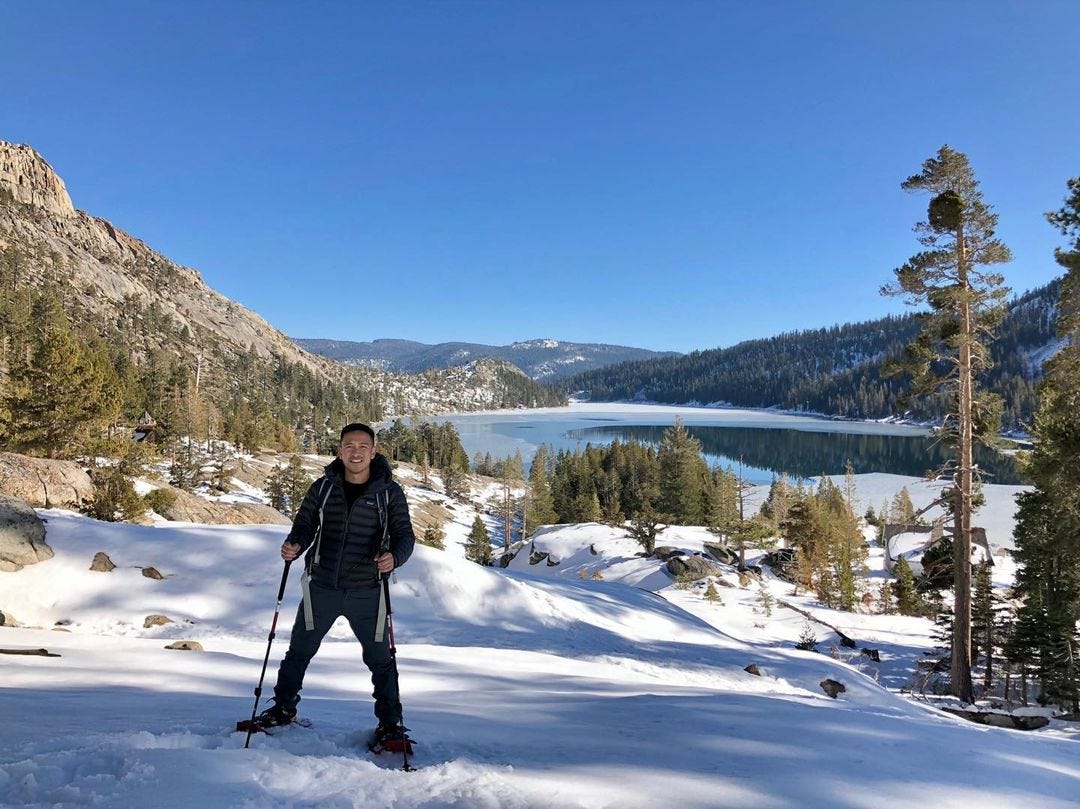A person posing wearing snowshoes and carrying hiking poles with Lake Tahoe in the background.