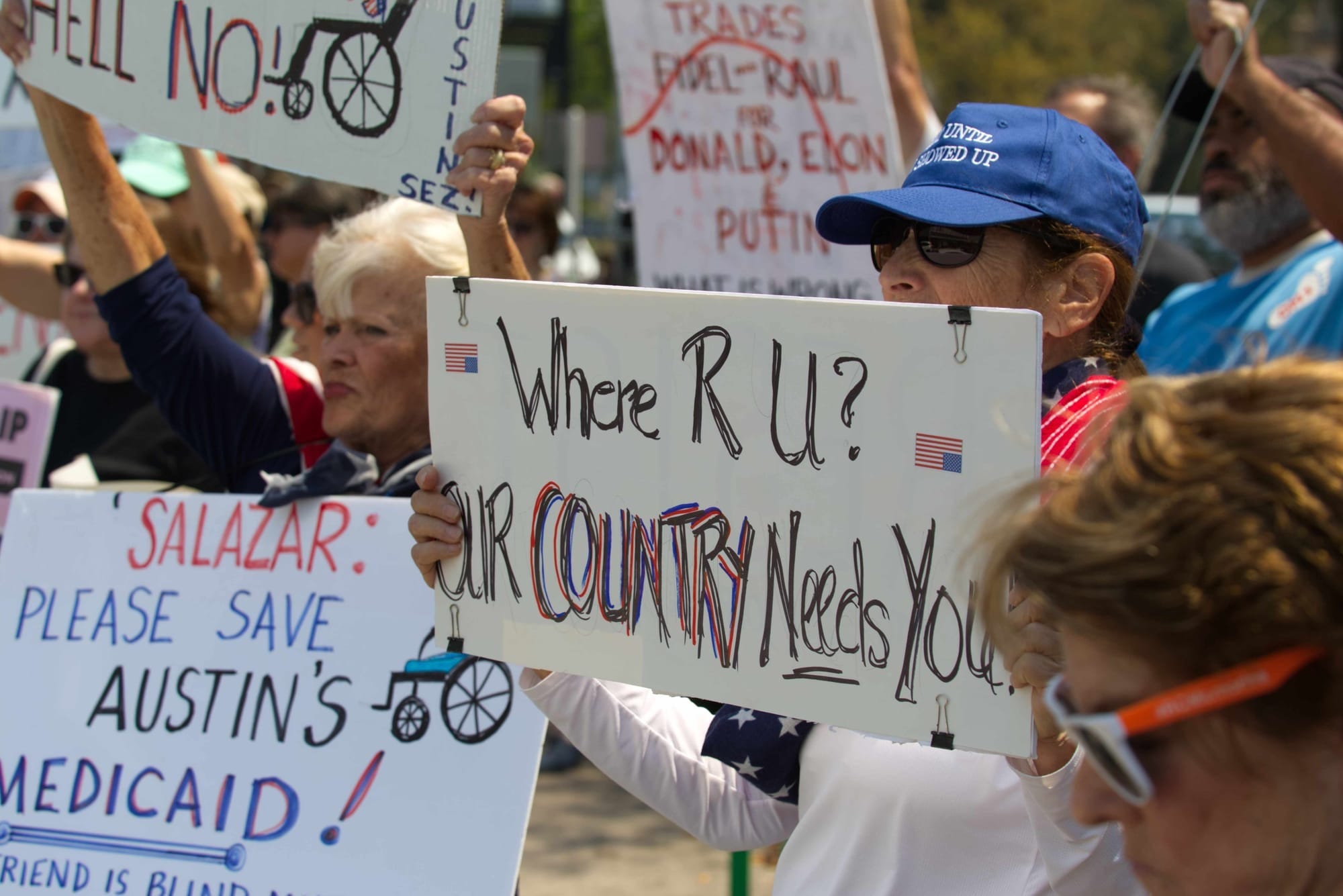 Several protestors hold up signs. The one in the center reads "Where R U? Our Country Needs You"