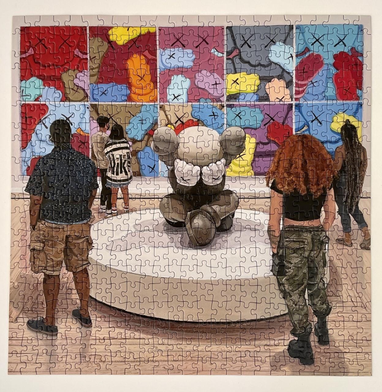 Completed jigsaw puzzle depicting museum visitors gathered around a seated KAWSsculpture with colorful abstract paintings on the gallery wall behind them.