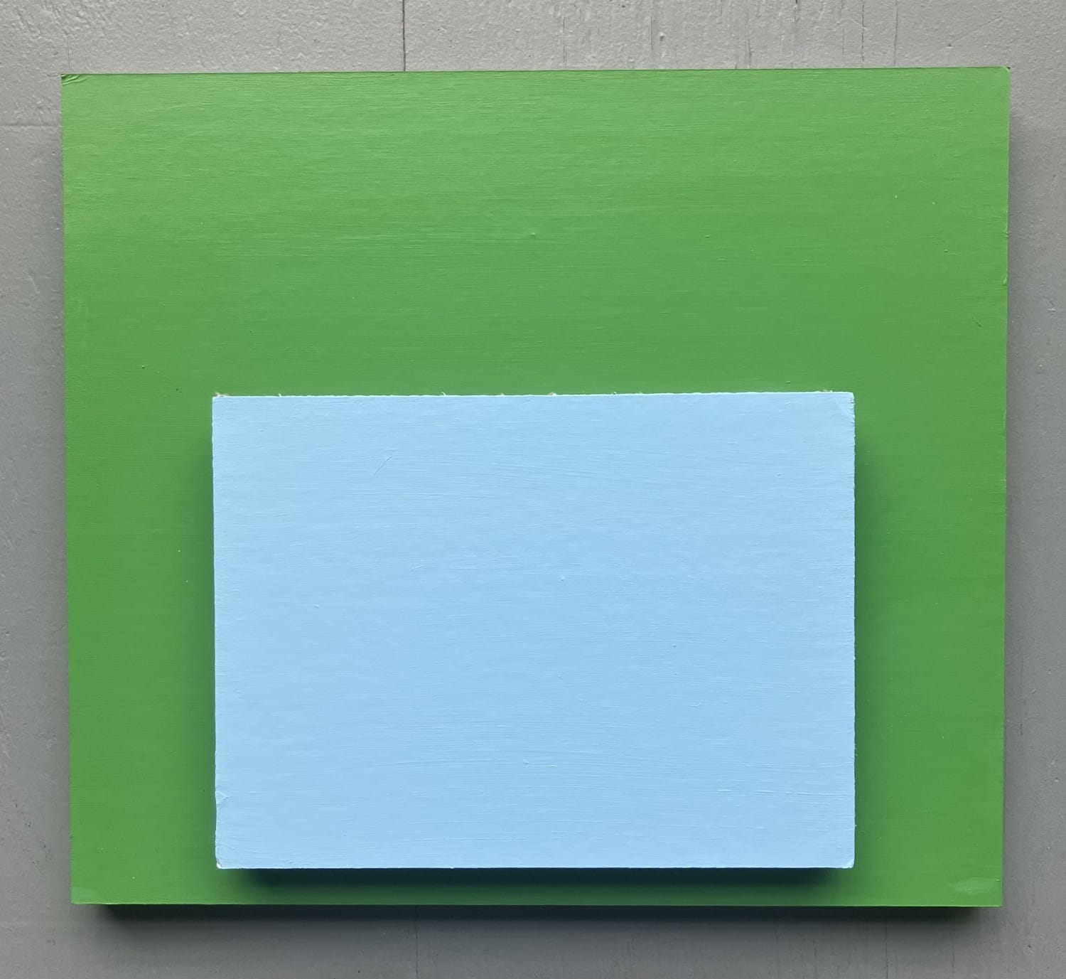 Minimalist painting with a light blue rectangular panel centered atop a larger green field, set against a gray background.