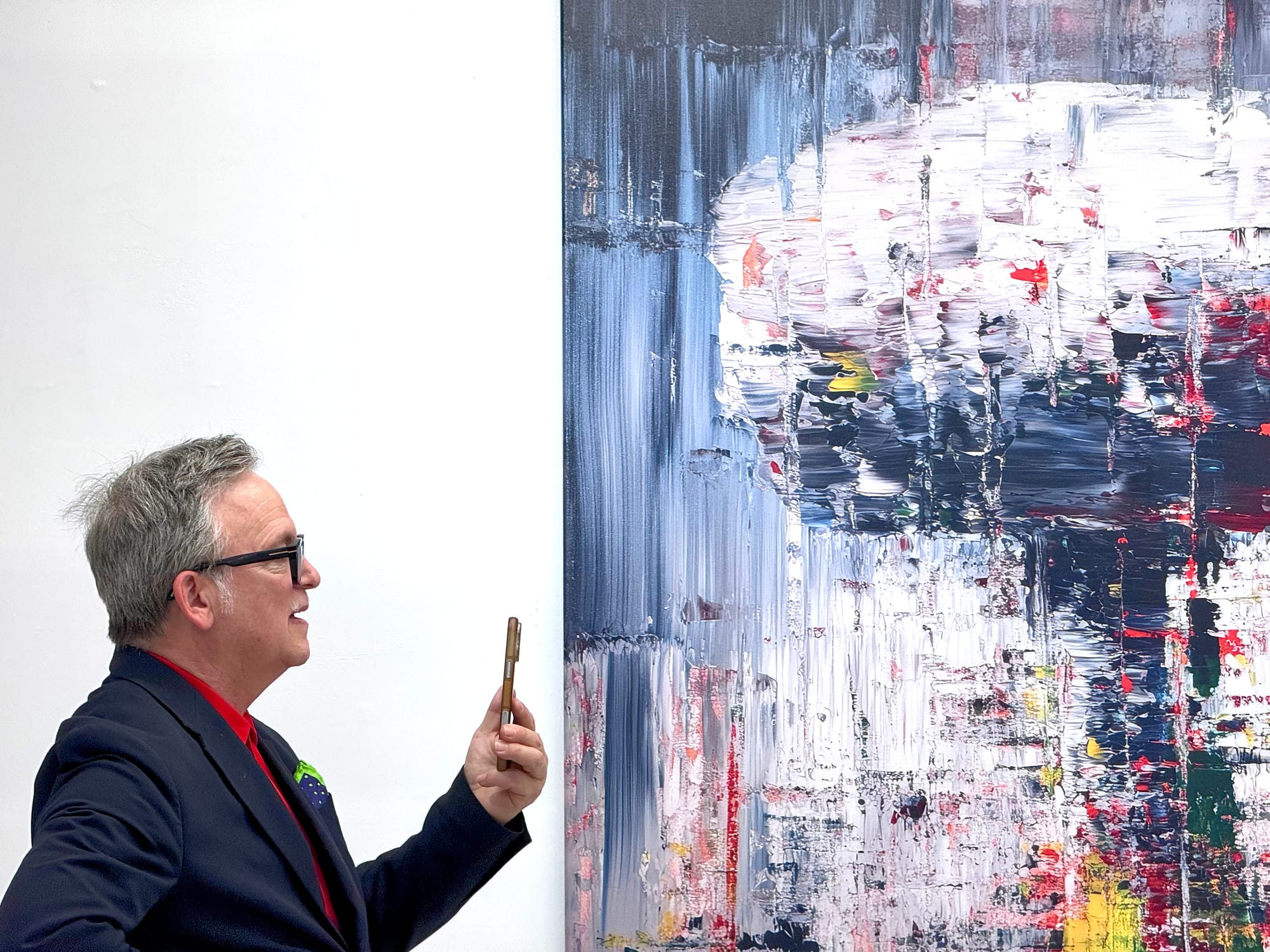 Gallerist Ethan Cohen holds his phone in front of an artwork by Marat Guelman, who is off-frame