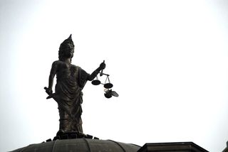 A bird flies past the scales of Lady Justice atop a courthouse dome