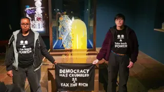 Two Take Back Power protesters stand beside the Crown Jewels display case at the Tower of London after custard and crumble were thrown on the glass
