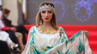 A woman wearing an Algerian ceremonial caftan with flowing fabric and traditional jewelry during a cultural event