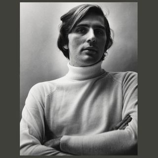 Stephen Koch folds his arms in front of his body in a black and white photograph by Peter Hujar