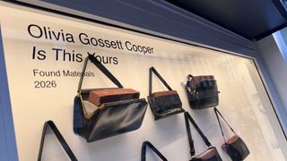 Purses with bricks are seen in an art display in a window.