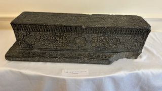 Timurid cenotaph from Uzbekistan displayed on a white tablecloth, with carved Arabic inscriptions and decorative geometric patterns visible on the dark stone surface.