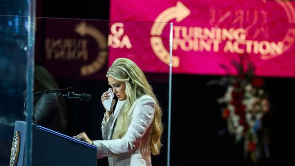 A woman wipes tears from her eyes at a podium with the Turning Point logo in the background