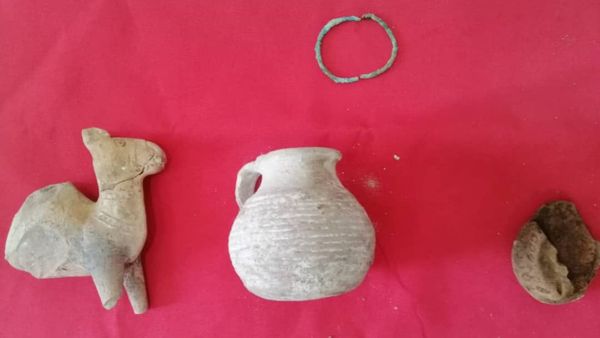 Three small antiquity-like objects displayed on a red clot  with a thin greenish metal bracelet or ring positioned above them.