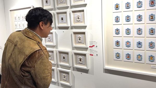 A visitor examines Richard Hoffman’s miniature paintings over postage stamps displayed in a grid at The Other Art Fair in Brooklyn.