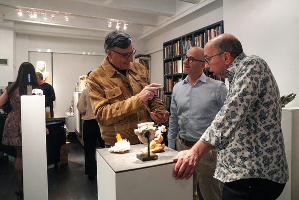 Three men stand around a pedestal displaying mineral specimens at an exhibition