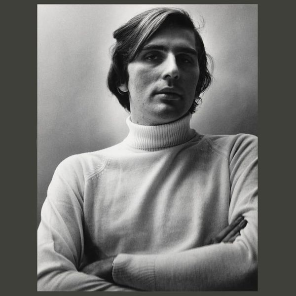 Stephen Koch folds his arms in front of his body in a black and white photograph by Peter Hujar