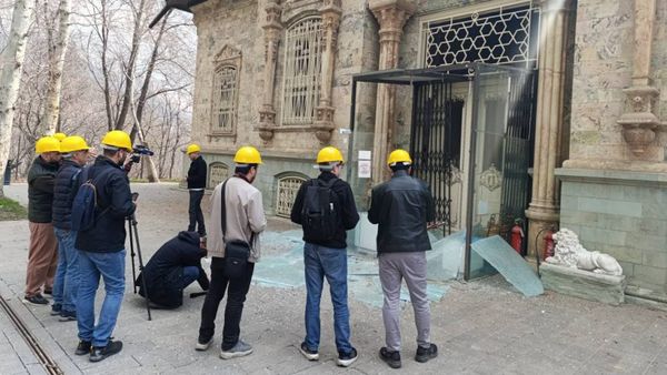 Group of people in yellow hard hats examine shattered glass outside a historic stone building at the Sa’dabad Complex in Tehran.