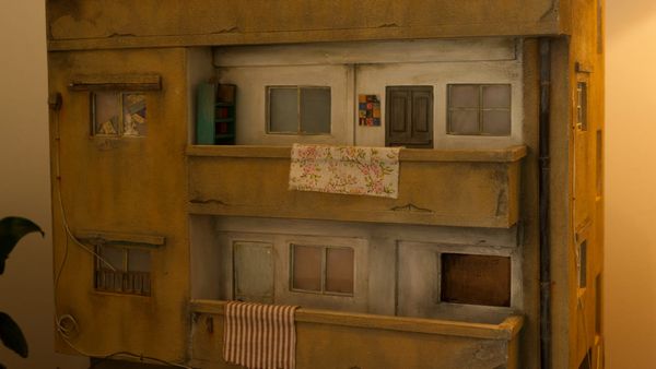 Detailed model of a multi-story building with balconies, small windows, and hanging fabric, part of Basel Zaraa’s Dear Laila installation.