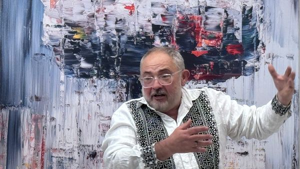 Marat Guelman, exiled from Russia, gestures with his hands in front of an artwork of an atomic bomb in the style of Gerhard Richter